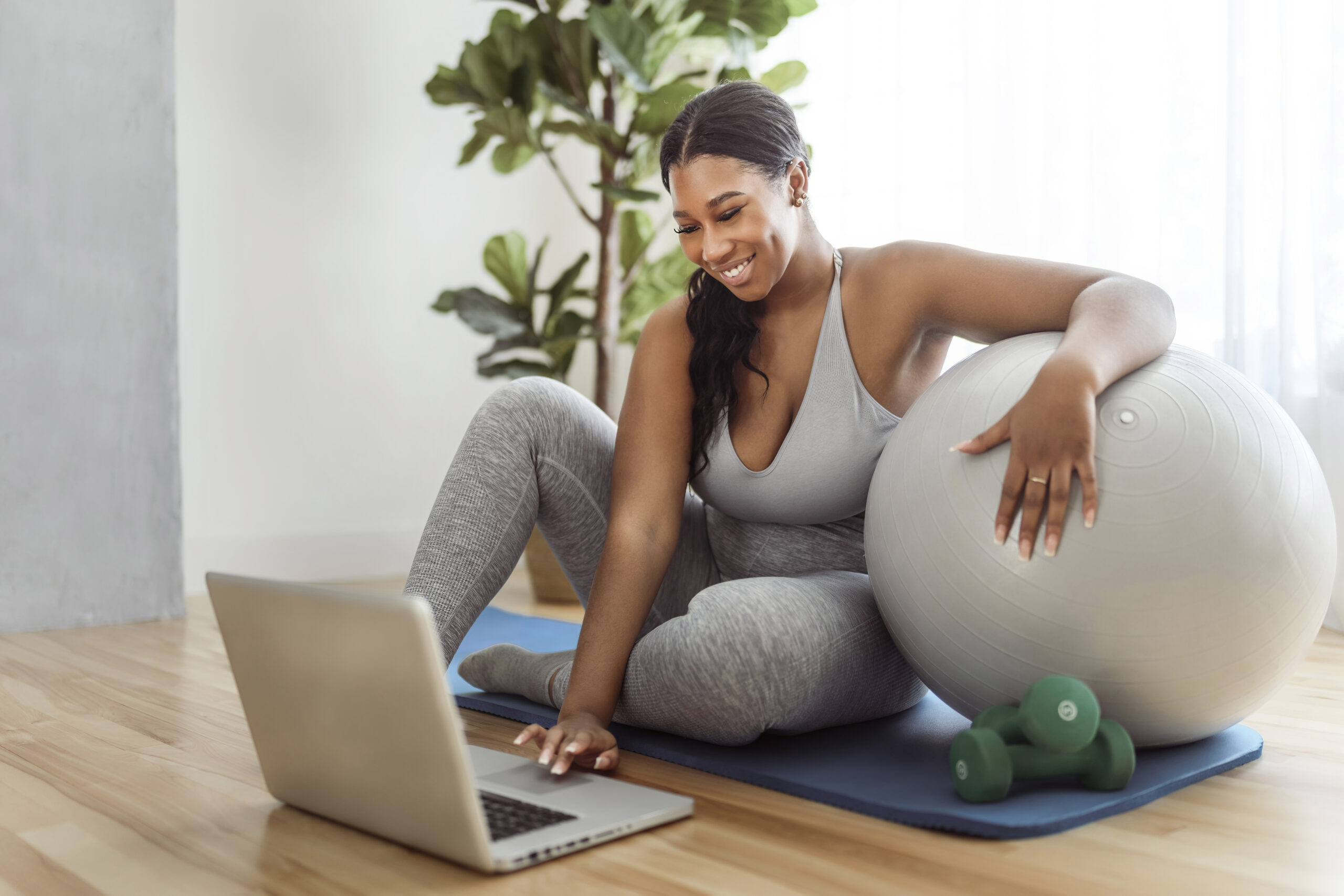 An African american woman working out in home livingroom gym with laptop