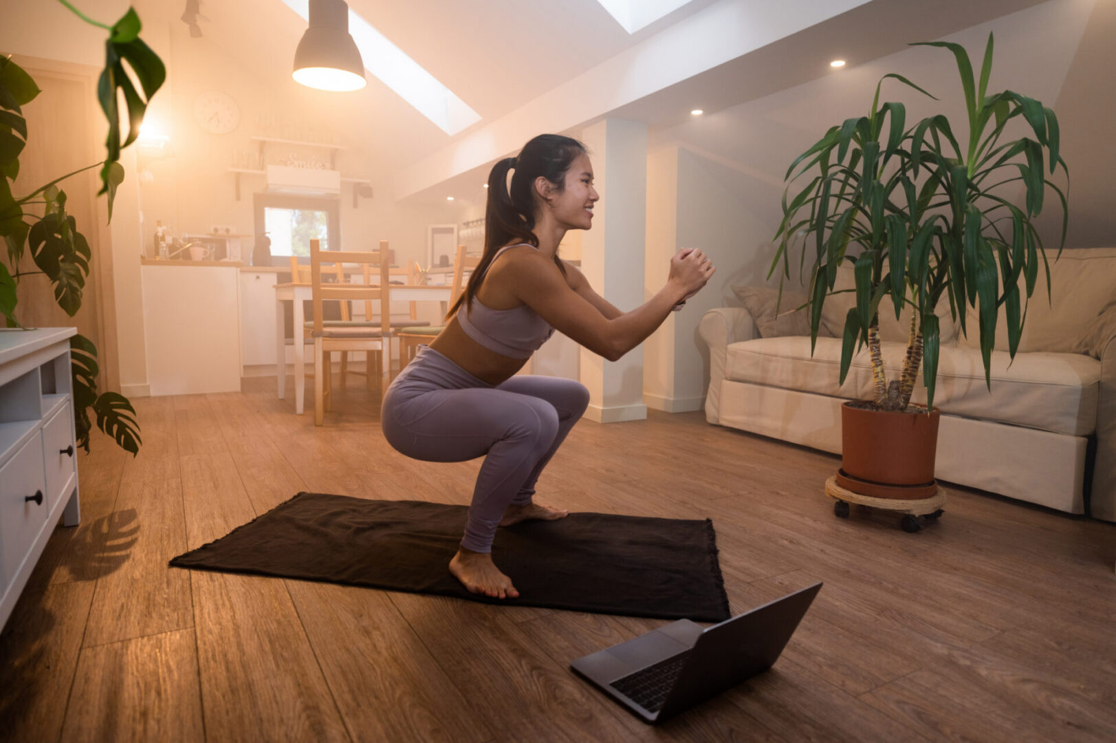 Fit Vietnamese woman in fitness clothes using online personal fitness trainer service on laptop and doing cardio exercises on fitness mat at home. Asian female doing exercises good physical shape.