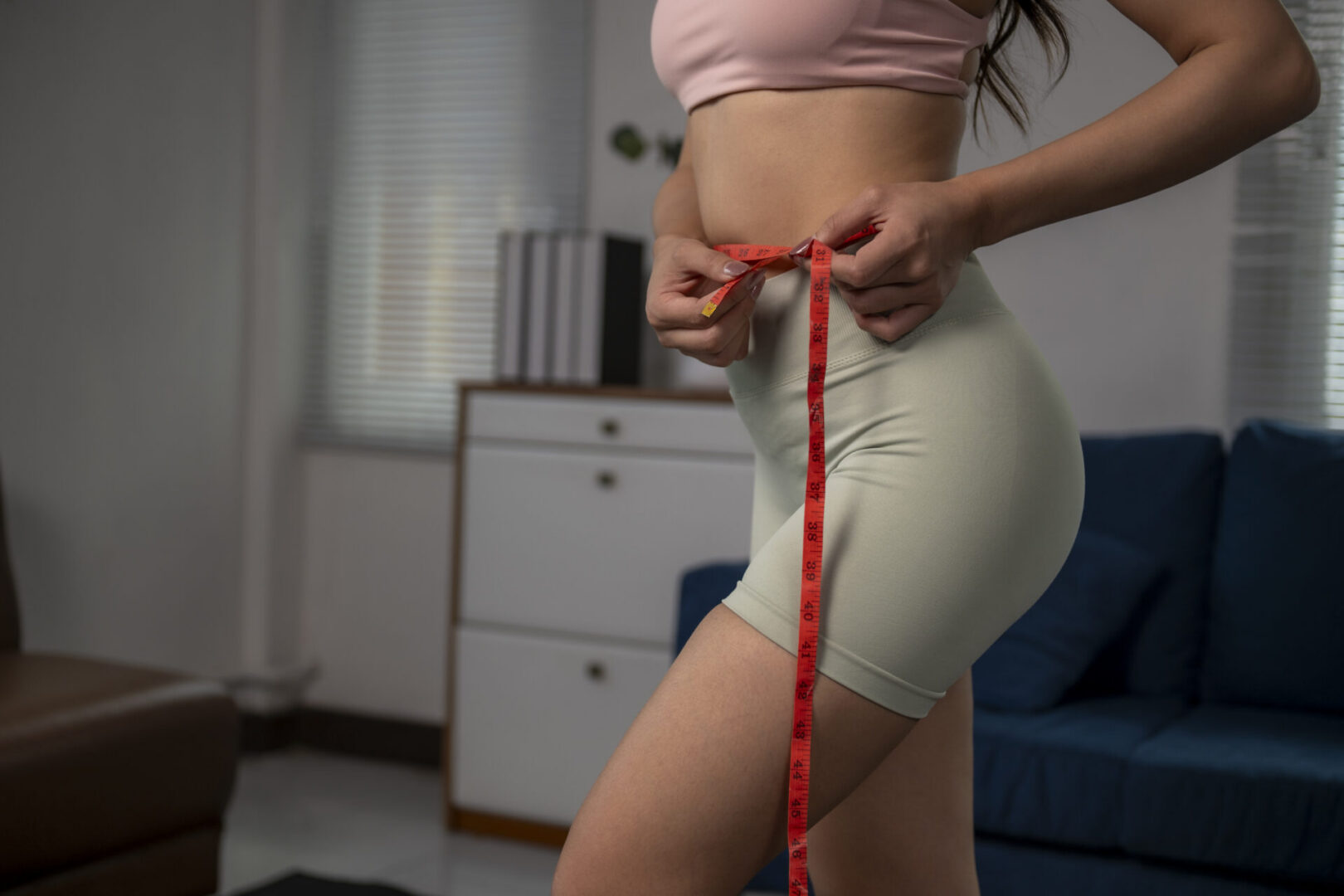 Woman measuring waist with red tape for fitness and health monitoring at home