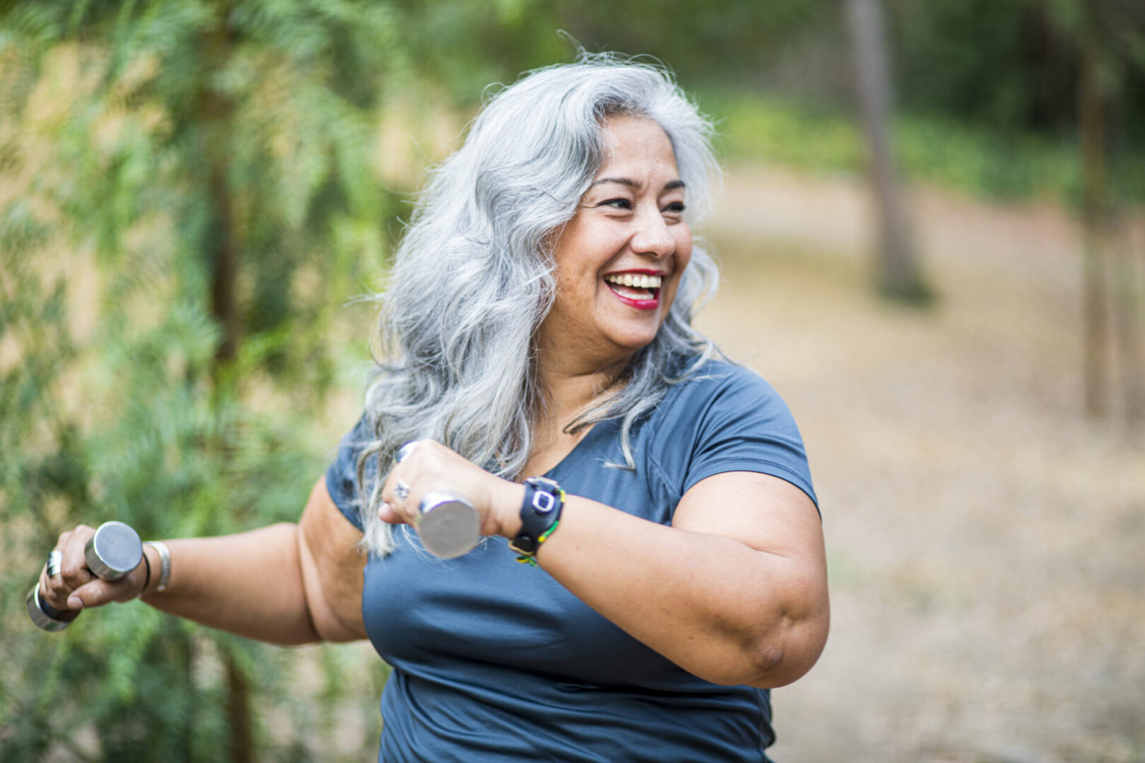 Smiling gray-haired woman exercising with dumbbells outdoors