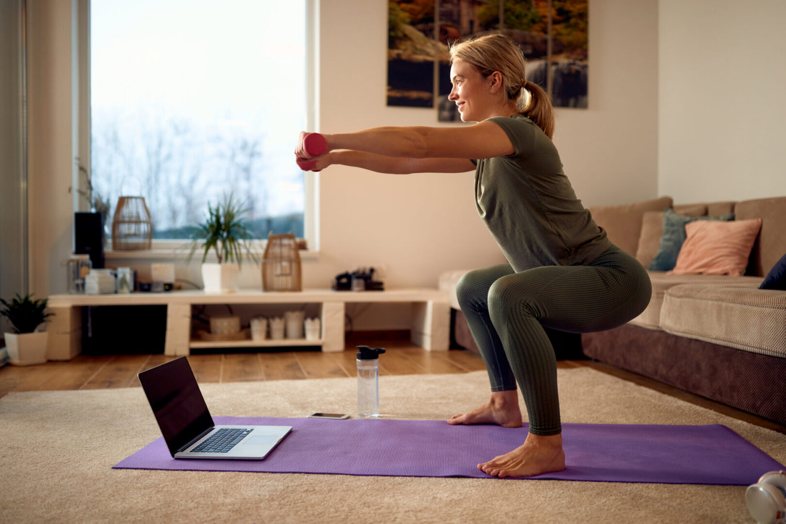 Happy sportswoman practicing squats while using hands weights during home workout.